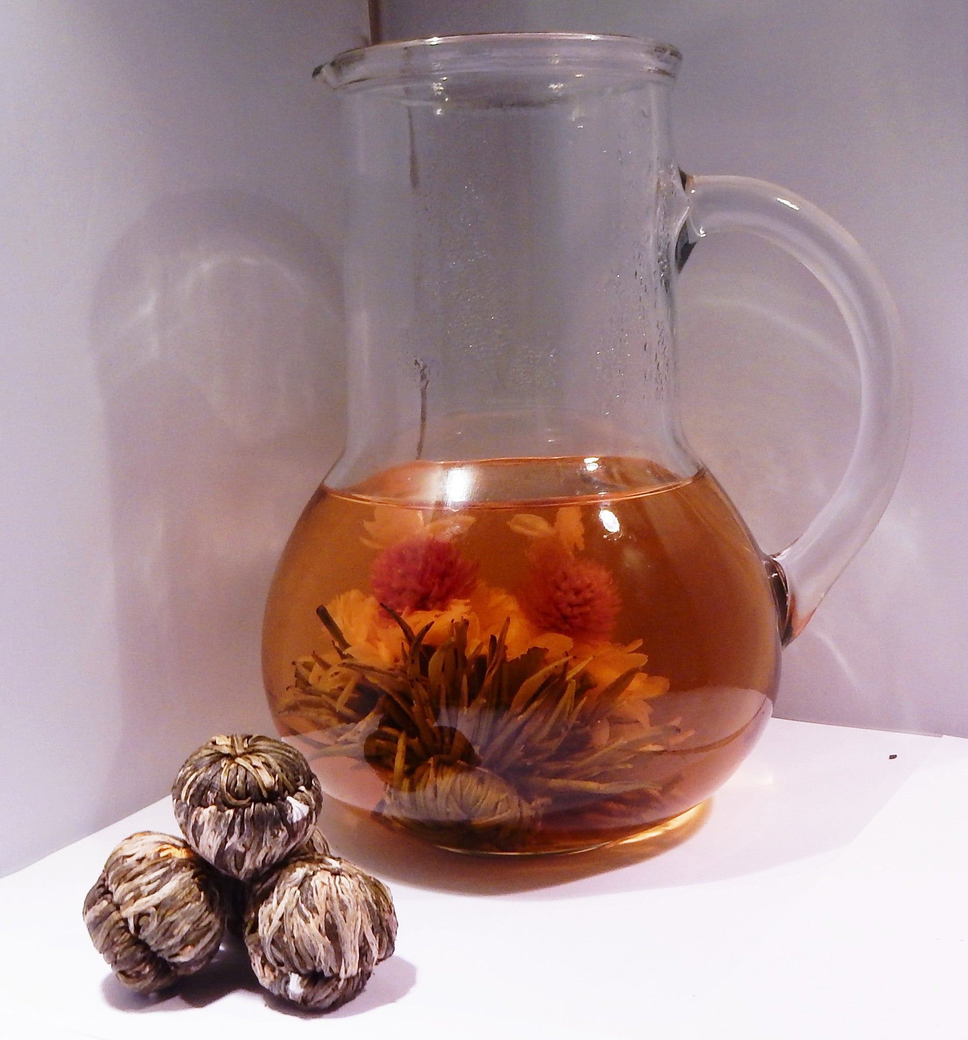 Double Happiness Chinese Green Tea - A pitcher of tea with a blooming tea ball inside and a pile of blooming tea balls to the bottom left