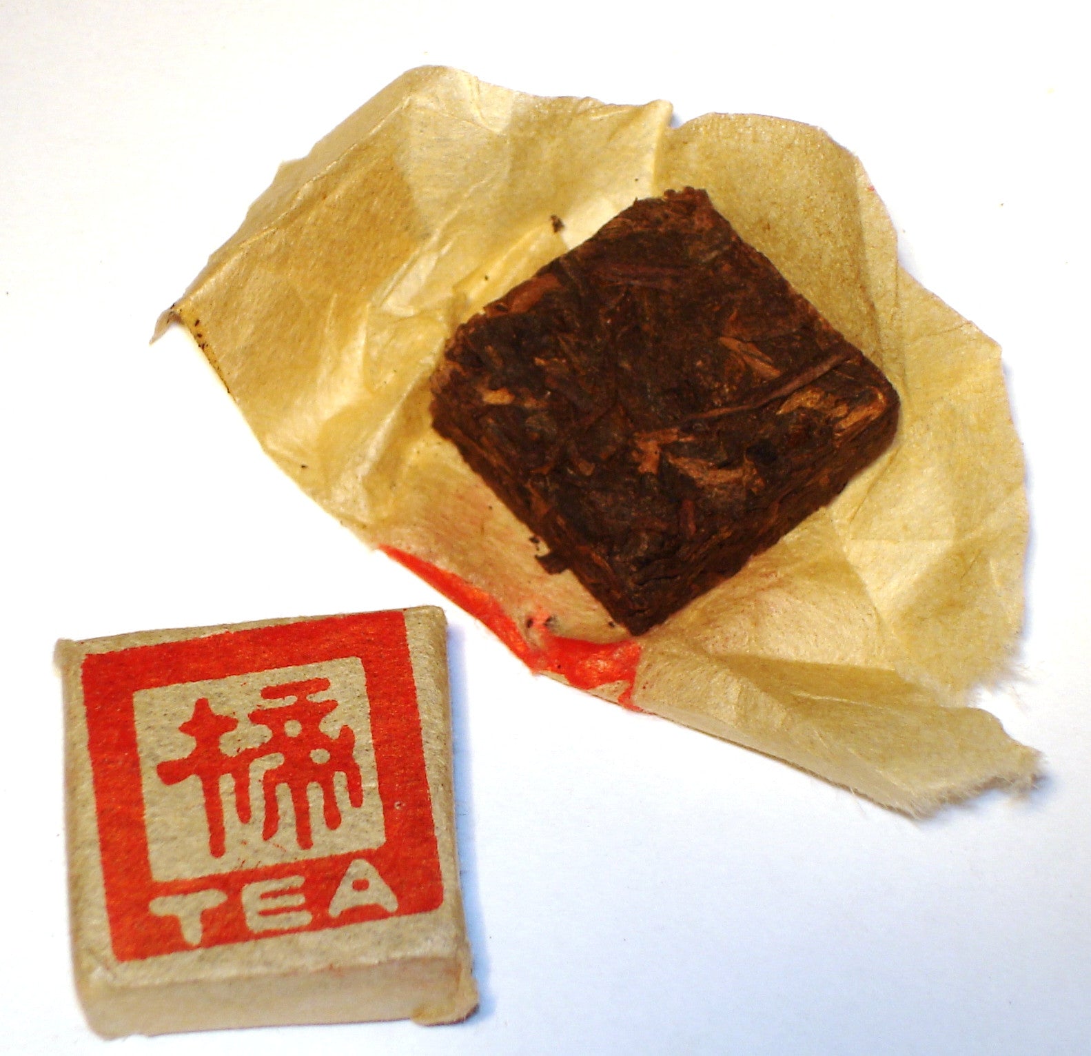 Mini Fangcha Chinese Shou Pu-erh tea brick in an open package, next to a sealed beige package with red characters